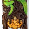 The Wood Ganesh Statue Wall Hanging is a vibrant wooden panel featuring Ganesha, the elephant-headed deity, seated and holding objects. He is framed by an ornate arch and flanked by two birds, perfect as Hindu Temple Decor or Pooja Home Decoration. Ready to ship.