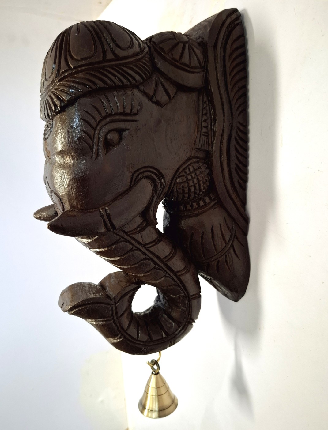 The Wooden Elephant Head Big Corbel features an intricately carved head and a quality brass bell hanging from its trunk. This Indian wood carving adds charm and elegance, creating a stunning decorative duo with its paired counterpart. Ready to ship vintage-style wall hanging decor.
