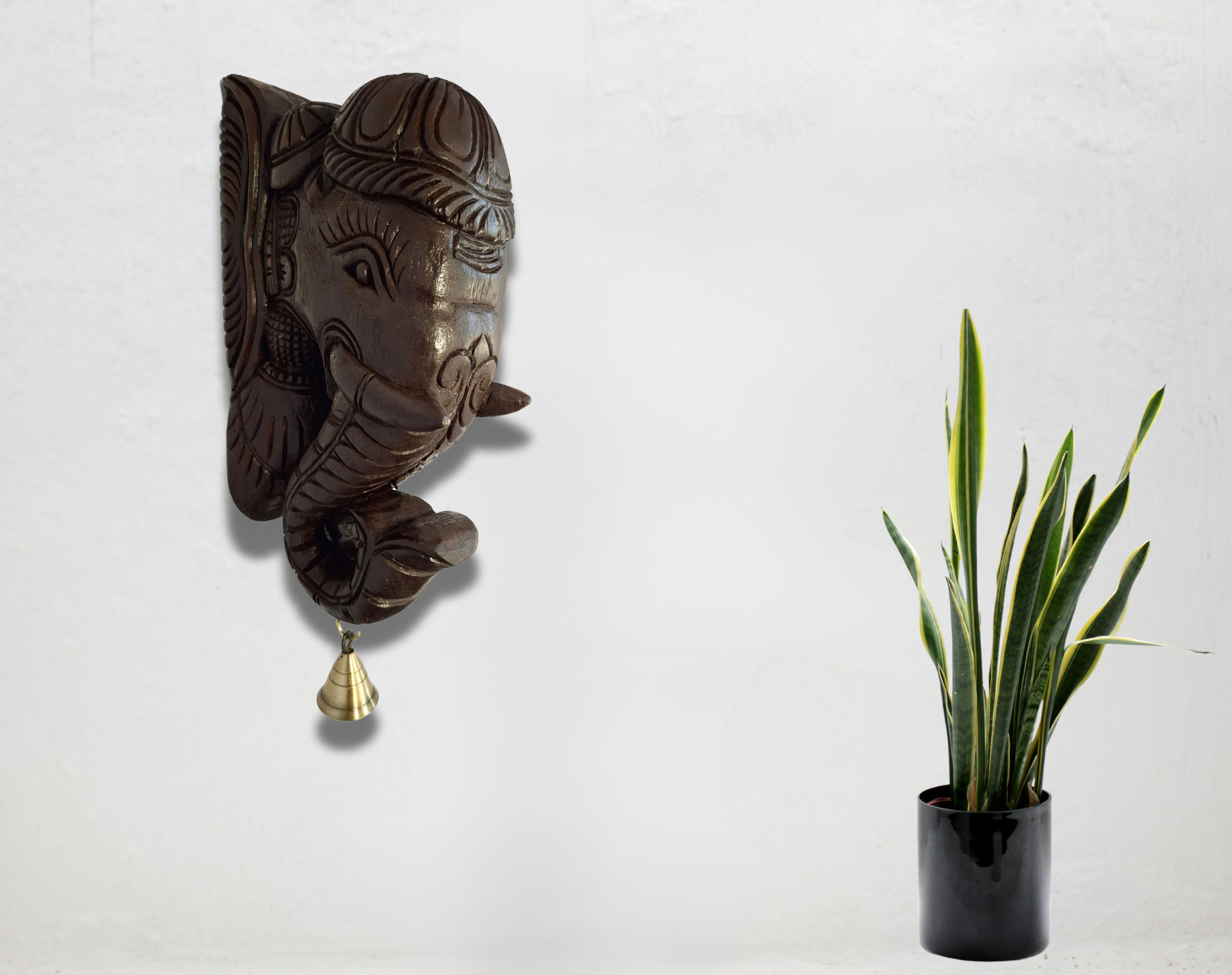 Featuring the Wooden Elephant Head Big Corbel with a quality brass bell, this captivating wall-mounted sculpture is paired with a potted snake plant on a white background. As part of an Elephant Wall Bracket Pair, it adds charm and elegance to any space.