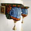 Wooden corbel pair mounted beside doorway with hanging diya and flowers