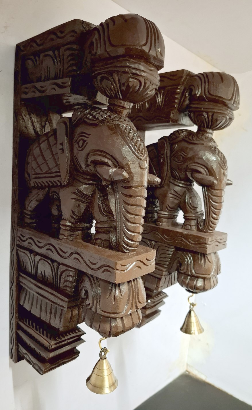 A pair of 18 inch wooden elephant corbels by JLine Arts with an antique look finish. Each hand-carved wall bracket features intricate detailing and hanging brass bells, ideal for door entrance wall decor.