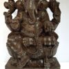 The Wooden Ganesha Statue, a 18-inch large sculpture named Ganapathi Vinayaka Vigneshwara, features Ganesha cross-legged with four arms holding items like a conch shell and axe. Adorned on a decorative pedestal, this temple figurine captures attention with its intricate details.