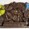 A wooden Ganesha wall panel features the deity reclining elegantly with intricate details and a crown, set against a floral arch. This Ganesh Statue combines traditional charm with exquisite craftsmanship, epitomizing artistry in its design.