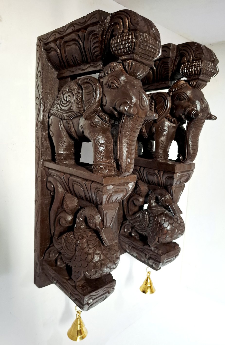 Set of 2 hand-carved wooden elephant and peacock wall brackets with brass bells. South Indian temple pillar design, antique brown finish. 18x9x3 inches each, 5.5kg total. Ready to hang. Perfect for puja room or housewarming gift.